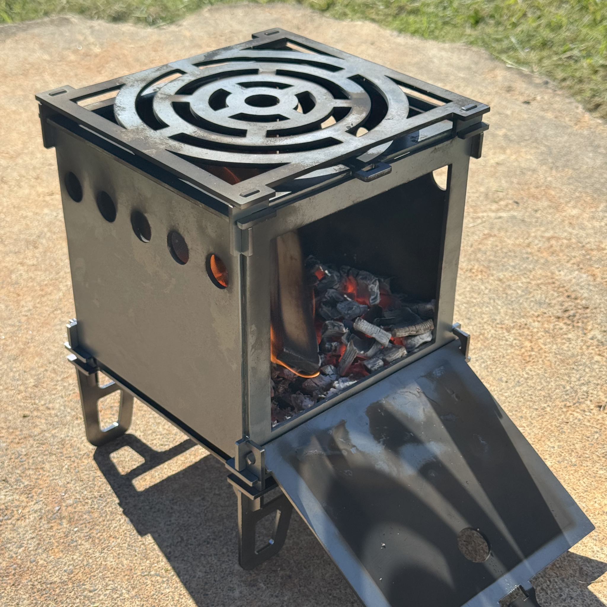 Portable metal stove with fire burning inside on a concrete surface