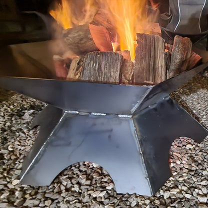 Metal fire pit with burning wood and flames on a gravel surface