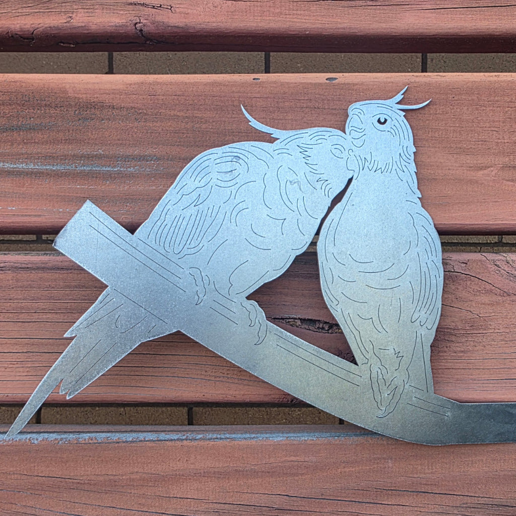 Metal sculpture of two birds on a branch against a wooden background